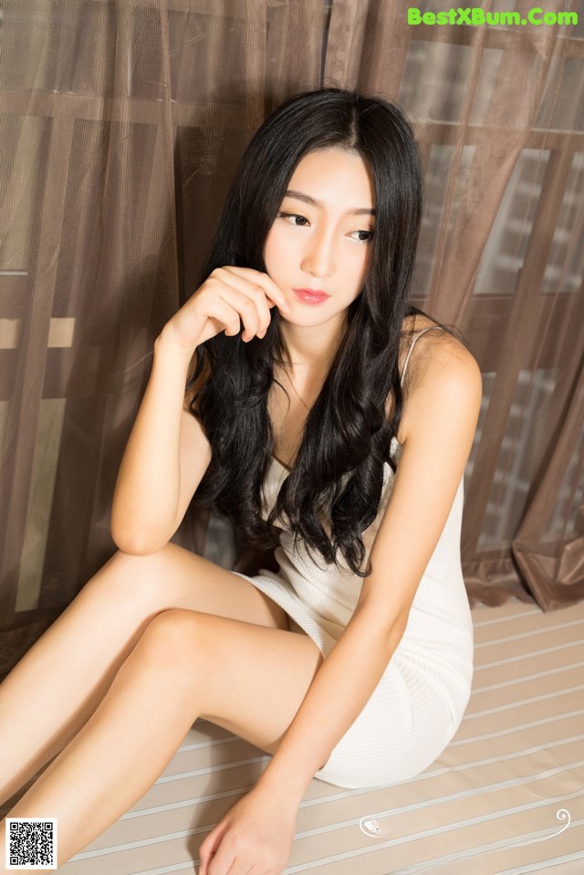 A woman in a white dress sitting on a bed.