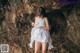 A woman in a white dress standing in front of a rock.