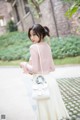 A woman in a pink top and white skirt holding a white bag.