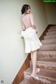 A woman in a pink top and white skirt is standing on some stairs.