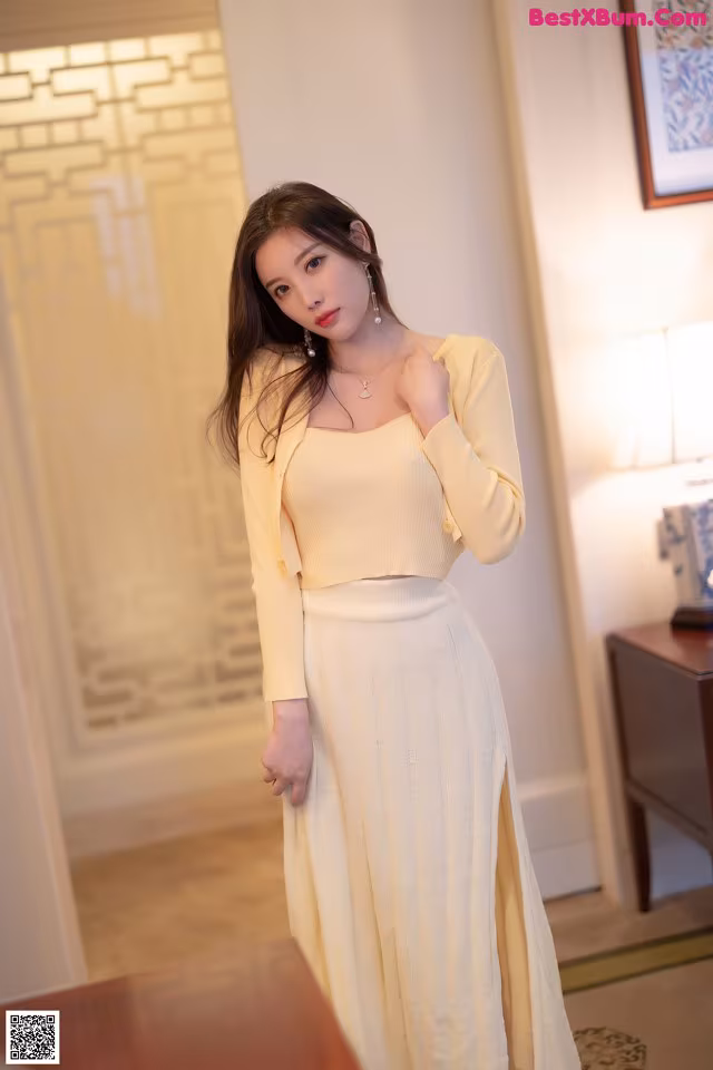 A woman in a yellow top and white skirt posing for a picture.