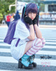 A woman with purple hair and glasses sitting on the ground.