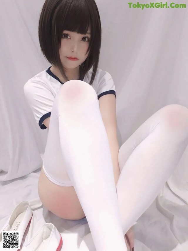 A woman in white tights and white shoes sitting on a bed.