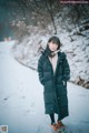 A woman standing in the snow wearing a black coat.