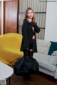 A woman standing in a living room holding a black bag.