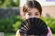 A woman holding a black fan in front of her face.