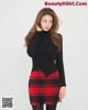 A woman in a black sweater and red plaid skirt posing for a picture.