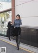 A woman walking down the street in a blue top and black pants.