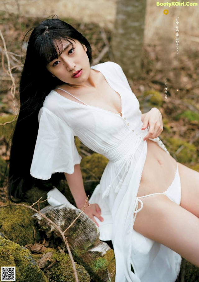 A woman in a white dress sitting on a rock.