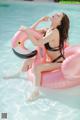 A woman in a black bikini sitting on an inflatable flamingo.