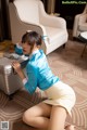 A woman in a blue shirt and yellow skirt posing with a suitcase.