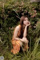 A woman in an orange polka dot dress sitting in the grass.