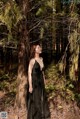 A woman in a black dress standing in the woods.