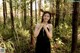 A woman in a black dress standing in the woods.