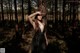 A woman in a black dress standing in the woods.