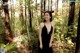 A woman in a black dress standing in the woods.