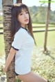 A woman leaning against a palm tree in a white shirt.