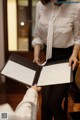 A woman in a white shirt and black skirt holding a folder.