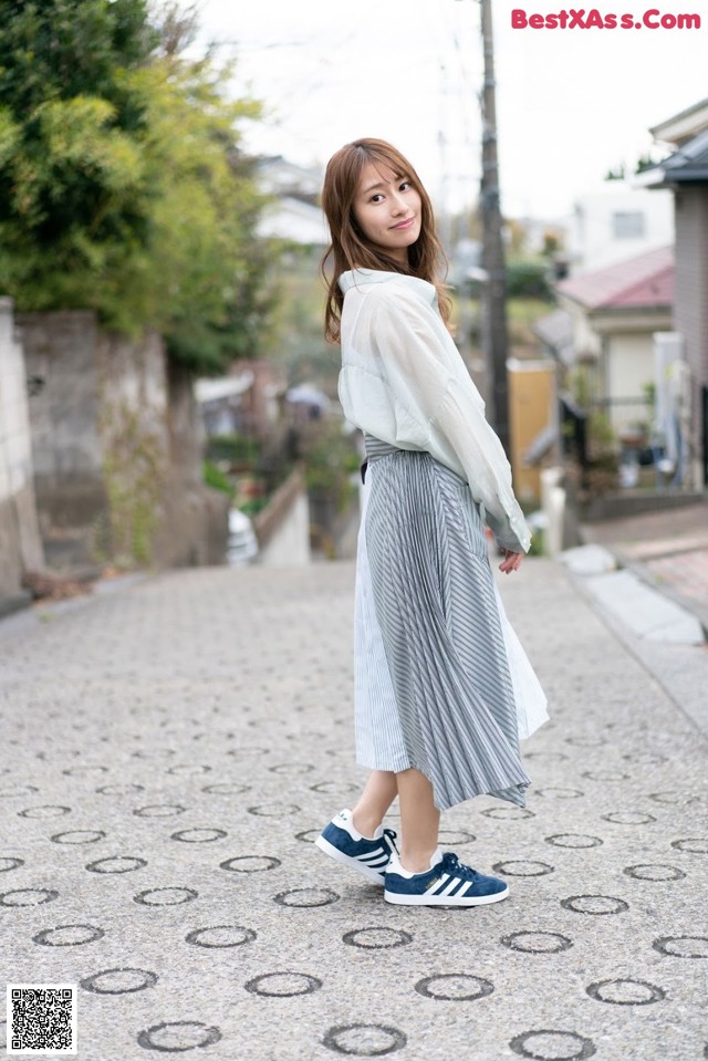 A woman in a white shirt and a gray skirt is walking down a street.