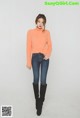 A woman in an orange sweater and jeans posing for a picture.