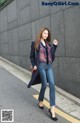 A woman in jeans and a coat is walking down the street.