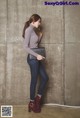 A woman leaning against a wall with her hand on her hip.