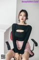 A woman sitting on a chair wearing a black top and pink skirt.